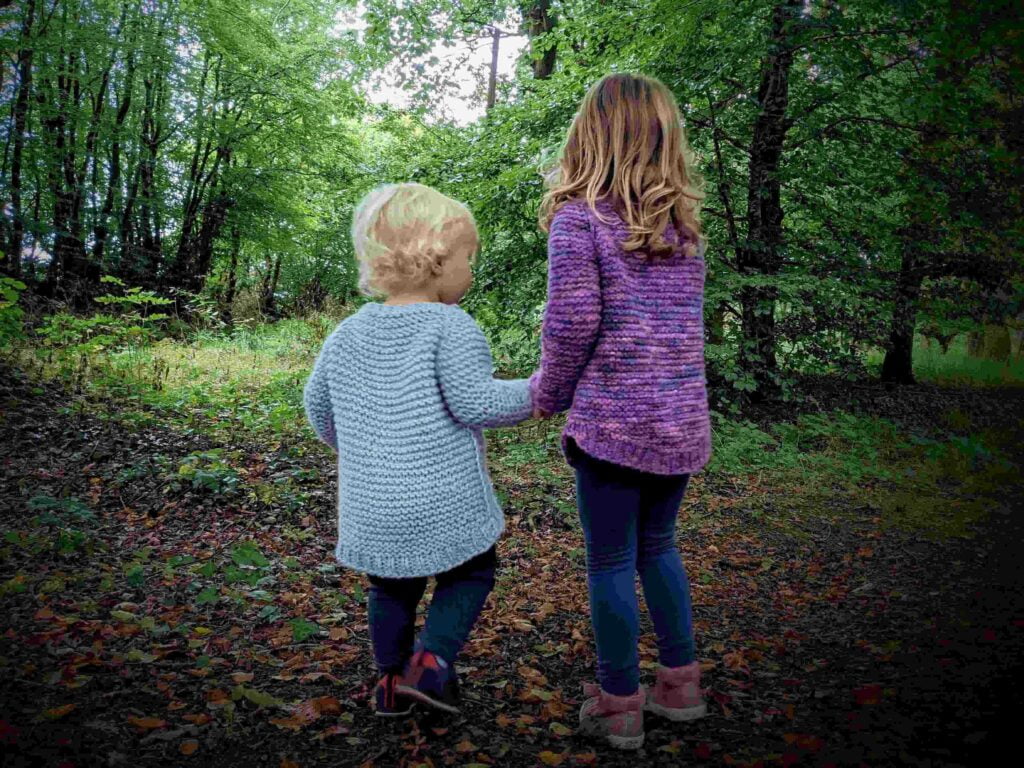 back view of two children wearing the garter squish kids jumper. on show is the all over garter stitch pattern and dropped back hems