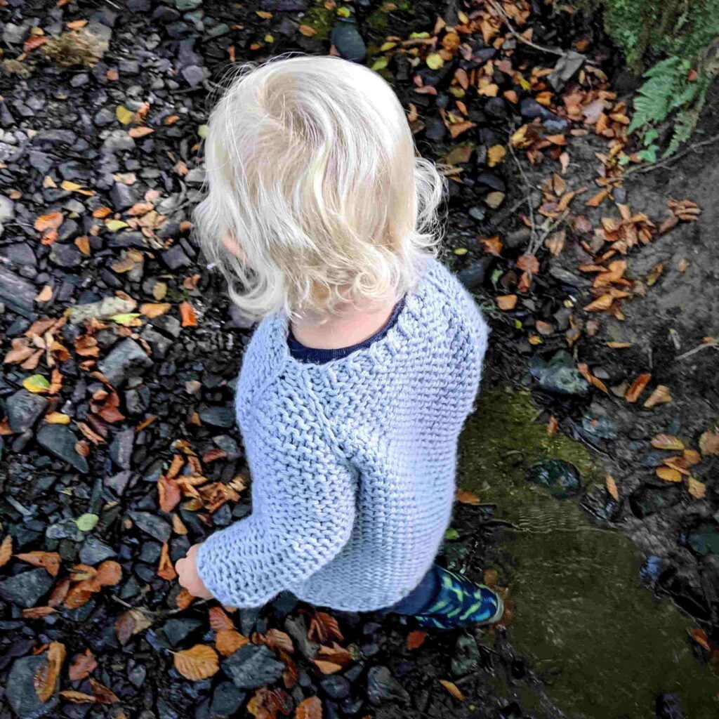 looking down to the neckline and shoulder of the garter squish kids jumper. shows the slip knit stitch raglan detail flowing from the ribbed hem. the rest of the jumper is knit in garter stitch