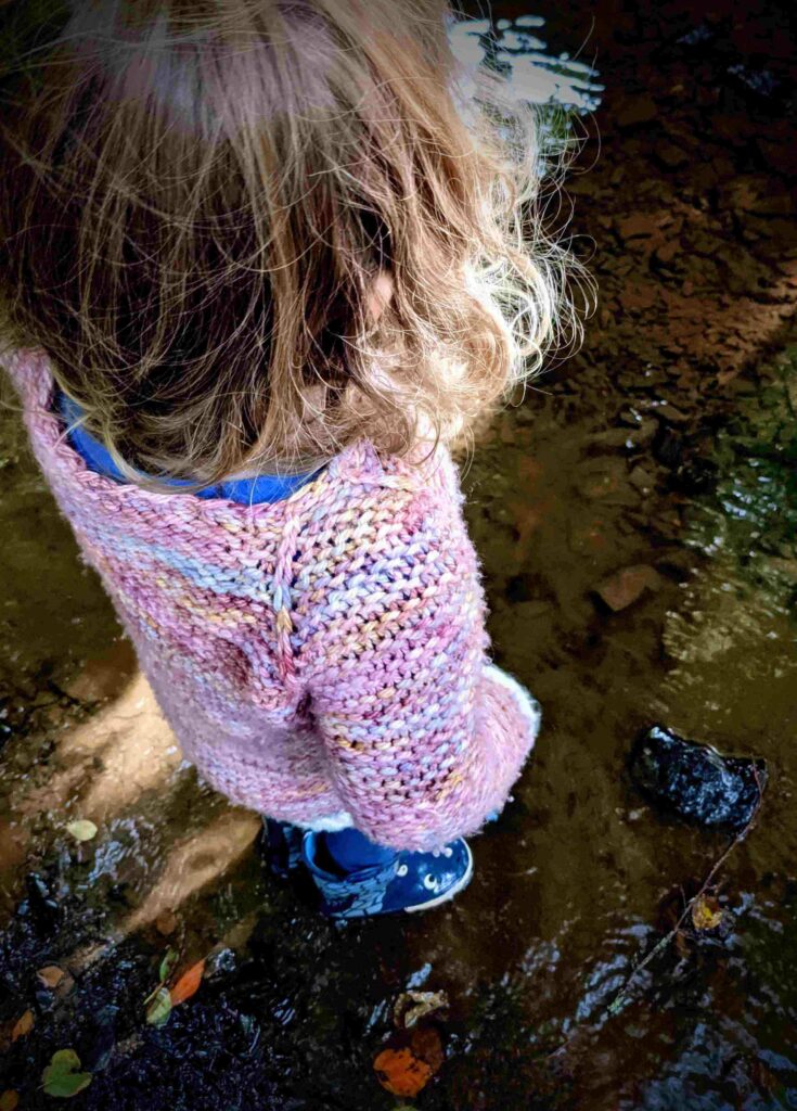 looking down to the neckline and shoulder of the garter squish kids jumper. shows the slip knit stitch raglan detail flowing from the ribbed hem. the rest of the jumper is knit in garter stitch