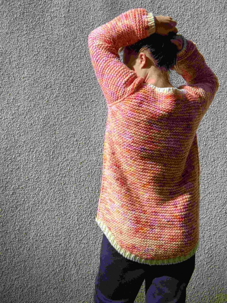 back view of the gater squish adult jumper shown on a woman. all over garter stitch, slipped knit stitch running through the raglan, sides and arms. the jumper has a dropped back hem on show