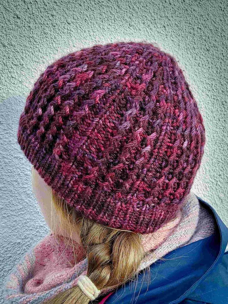 back view of the quinzhee beanie Knit from the top down, the quinzhee beanie features small zigzag like cables which make the hat very warm as squishy to wear. This beanie has a folded secured brim and is knit from a marron/wine coloured variegated hand dyed yarn