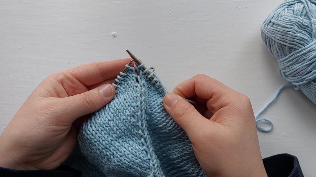 photo showing two hand holding some knitting with a make 1 left increase visible