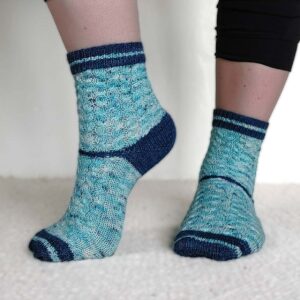 Image of the Poolside Socks being worn. Light blue cabled socks with a dark blue contrast cuff, heel and toe.
