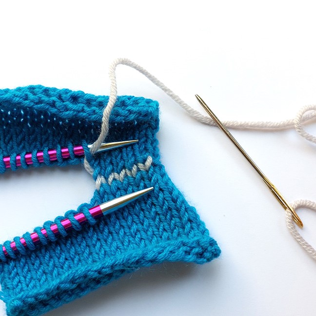 flatlay image of knitting stiches being grafted together using a darning needle